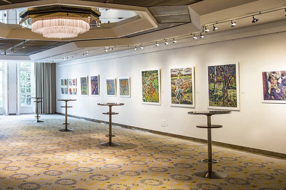 Galerie des Grand Elysée Hamburg mit zahlreichen Bildern, ein paar Stehtischen und einem großen Leuchter an der Decke