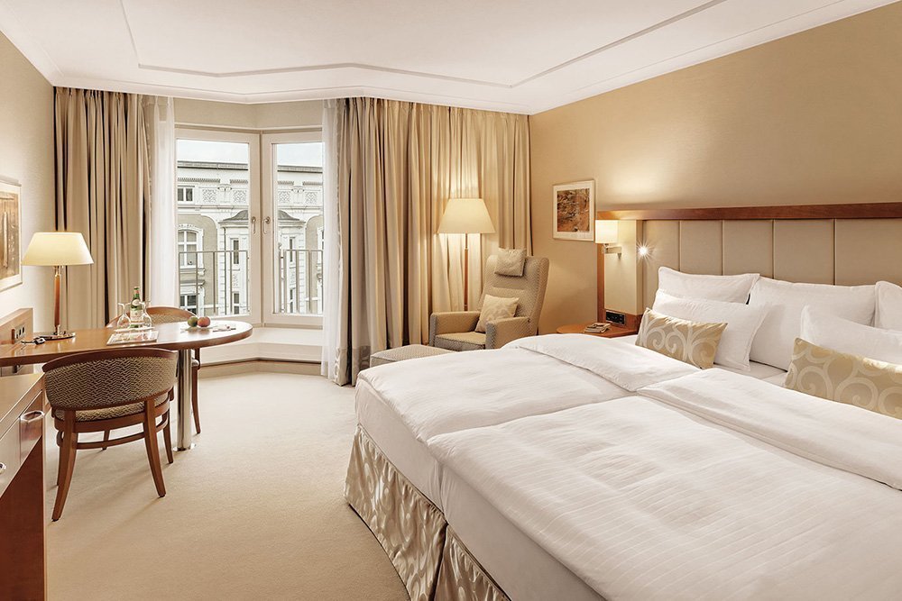 Luxuriöses, weiches Doppelbett in cremefarbenem Zimmer im Hotel Grand Elysée Hamburg mit Blick auf die Stadt