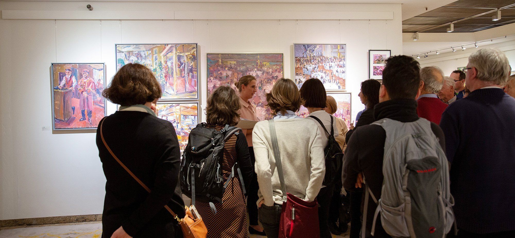 Gruppe von Menschen steht vor einer Bildergalerie im Grand Elysée Hamburg und hört einer Dame zu