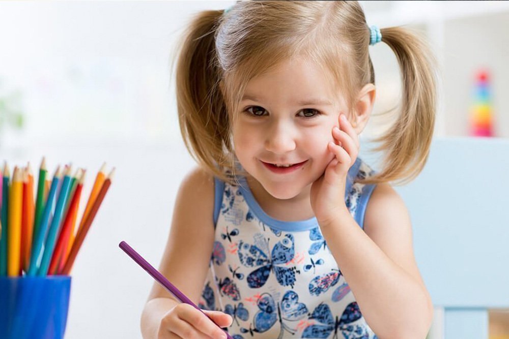 Kleines Mädchen lächelt in die Kamera und malt mit ihren Buntstiften ein Bild im Kindergarten des Grand Elysée Hamburg