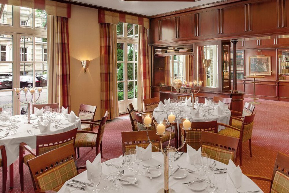 Bild des vorbereiteten Tagungsraums "Bibliothek" mit Kerzen und drei gedeckten Tischen im Hotel Grand Elysée in Hamburg