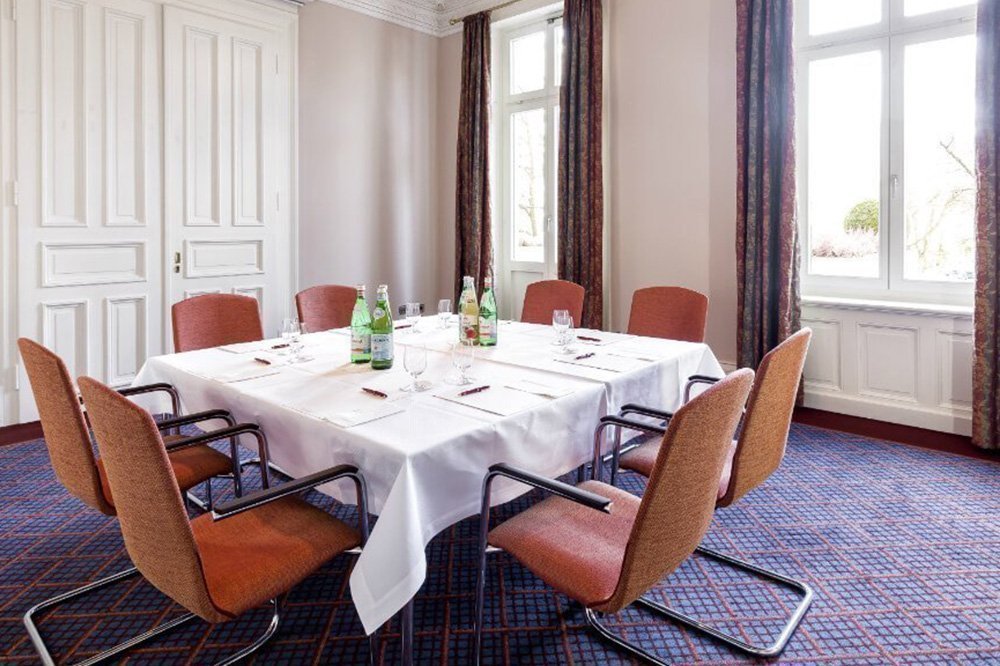 Tagungsraum "Poesldorf" in Hamburg mit hohen Decken, blauem Teppich und einem Meetingtisch mit acht Plätzen
