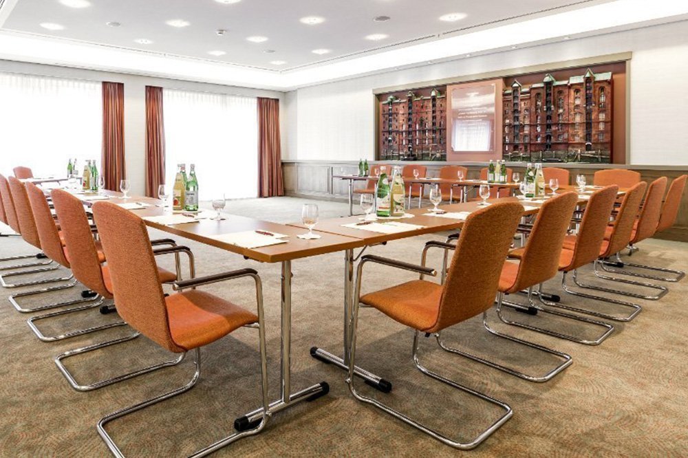 Weiß und braun gestalteter Meetingraum mit U-förmig angelegten Tischen, die mit Gläsern und Getränken gedeckt sind
