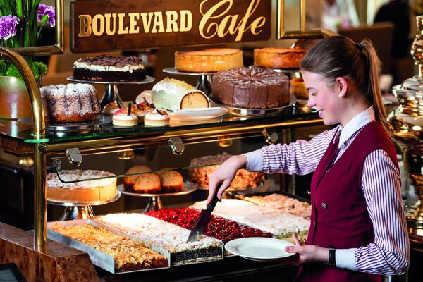 Mitarbeiterin nimmt einen Stück Kuchen aus der vielfältigen Kuchentheke im Boulevard Café in Hamburg im Hotel Grand Elysée