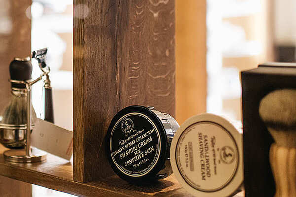 Rasierprodukte, wie Shavingcream und ein Rasierpinsel in einem dunklen Holzregal in der Boutique Stilhaus Blocker im Hotel Grand Elysée Hamburg