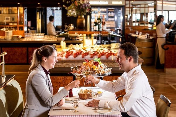 Am Tisch sitzendes Paar in der Brasserie Flum, welches zum Abendessen mit einem Glas Weiswein anstoßt