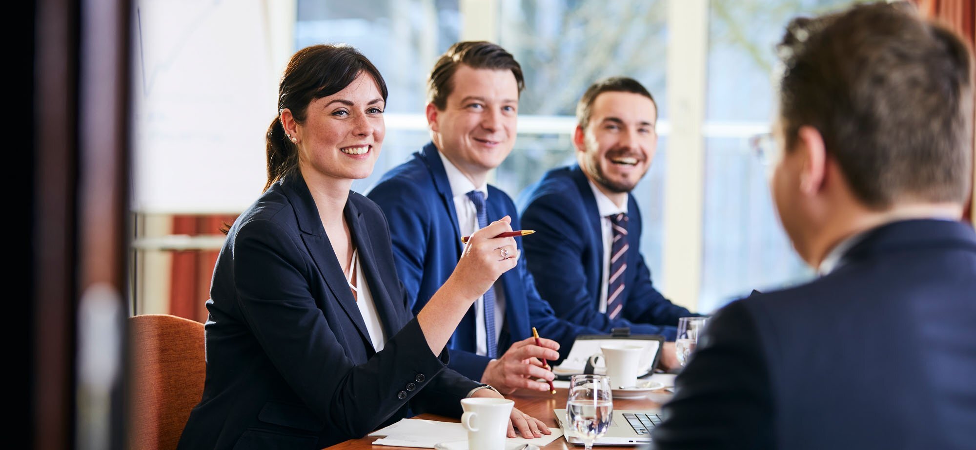Mehrere Personen in Businesskleidung sitzen zusammen an einem Tisch