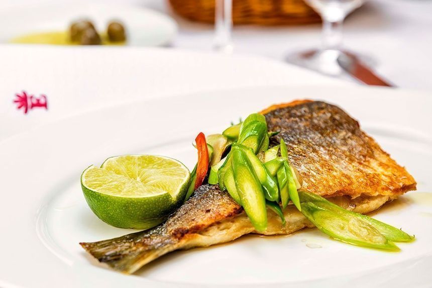 Ein Teller mit gegrilltem Fisch, grünem Gemüse und Limettenhälfte in einem Restaurant in Hamburg